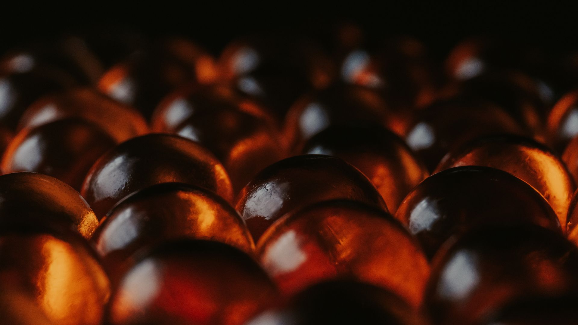 A close view of rows of translucent amber capsules packed together, each one lit from behind so the light runs through it